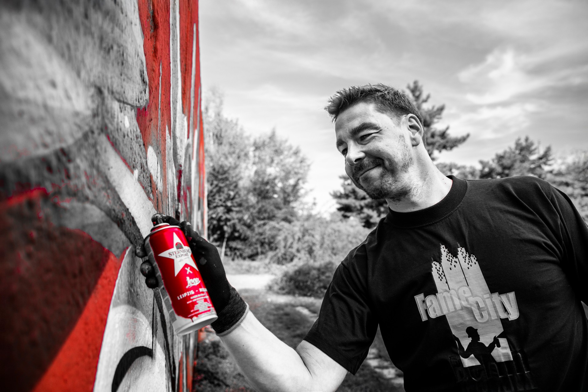 Mann steht vor einem Graffiti-Kunstwerk. Szene teils farbig, teils Schwarz-Weiß, mit Fokus auf die Sternburg Spraydose.