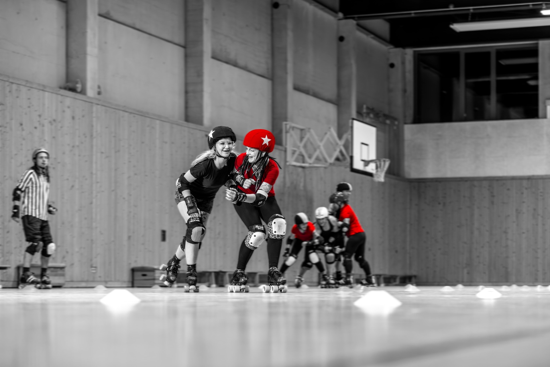 Fokus auf zwei Roller-Derby-Spielerinnen, eine in Rot, die andere in Schwarz, während eines Spiels in einer Sporthalle.