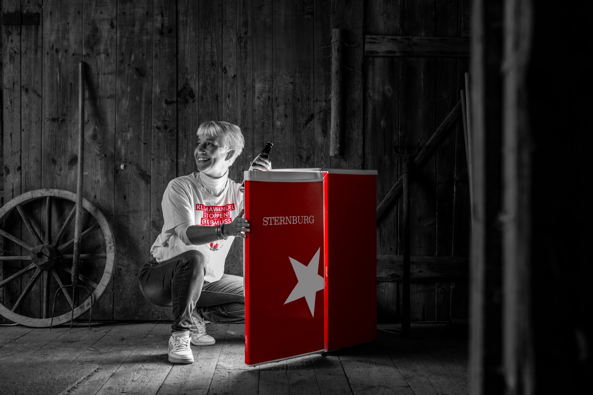 Eine Frau kniet vor einem Kühlschrank mit der Aufschrift Sternburg und entnimmt eine Bierflasche.