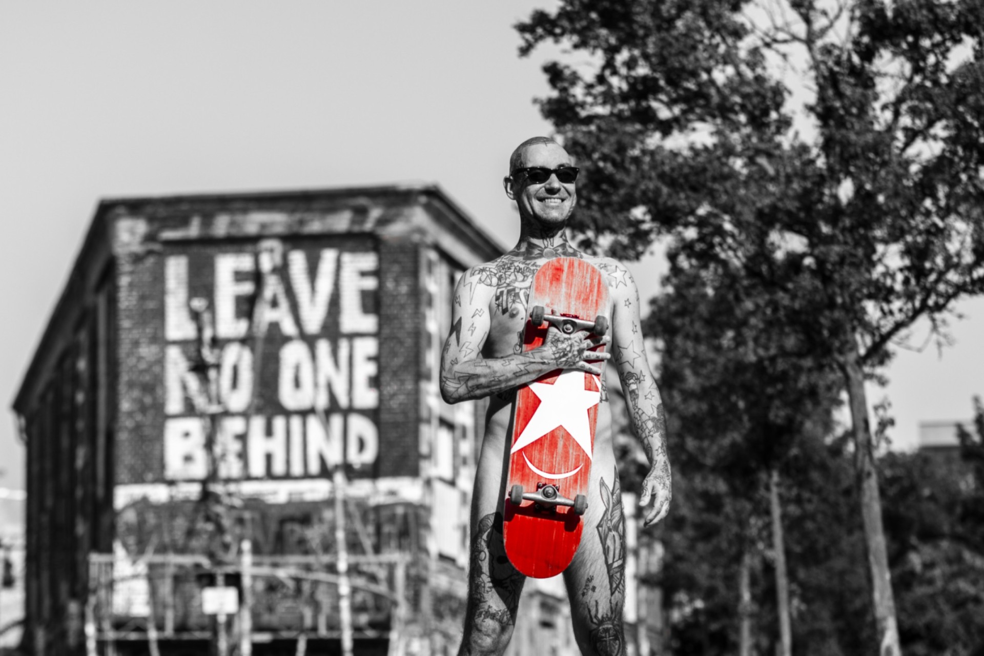 Ein Mann mit Tattoos steht vor einem Gebäude. Er hält ein rotes Skateboard mit dem Sternburg Logo.