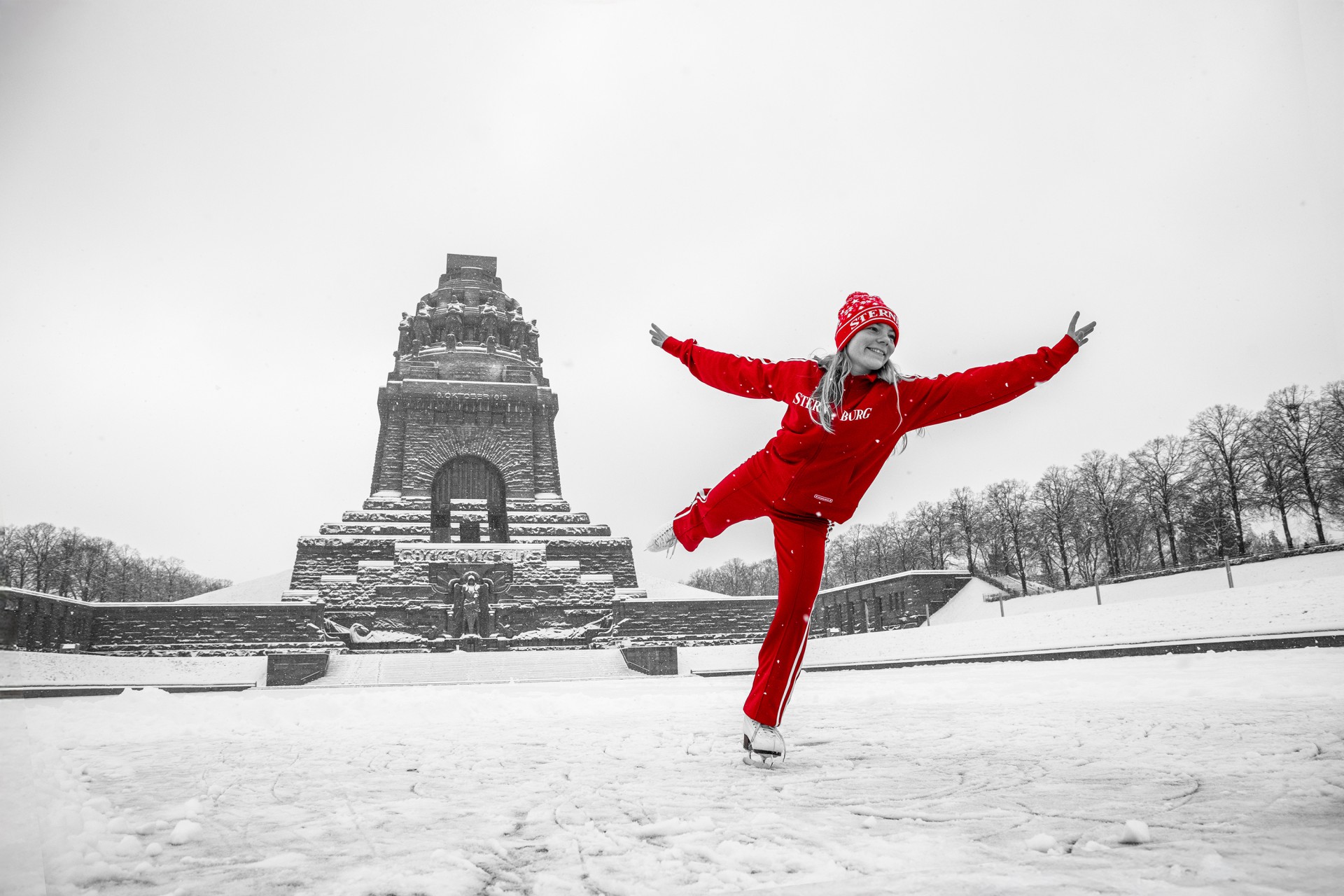Eine Frau in einem Sternburg Jogging Anzug fährt Schlittschuh vor dem Völkerschlachtdenkmal.