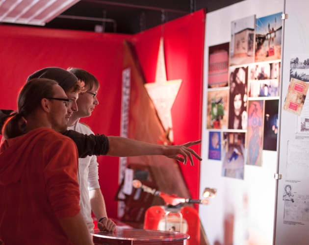 Zwei Personen betrachten und diskutieren Fotos und Objekte in einer Ausstellung.