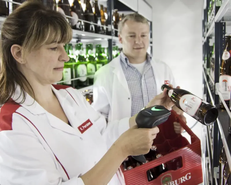 Zwei Personen scannen in einer Getränkeabteilung Flaschen mit einem Handscanner.