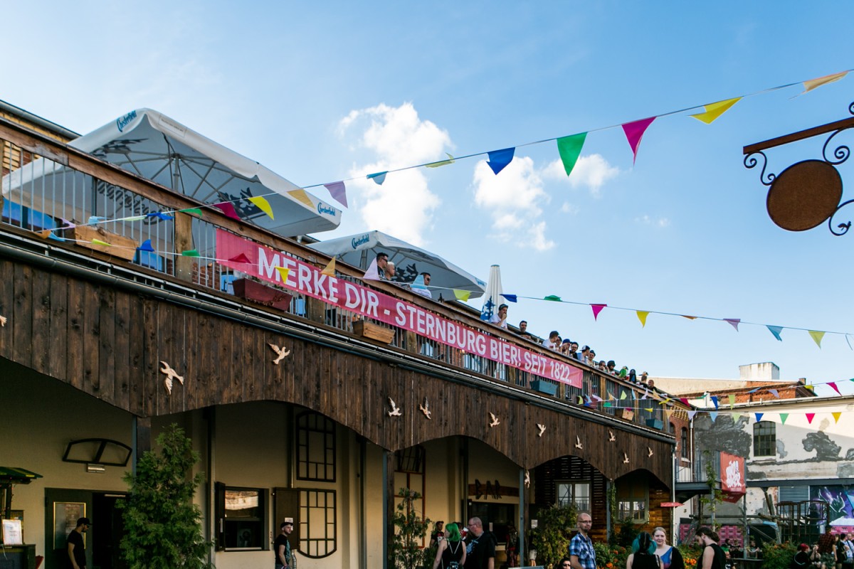 Menschen feiern auf Terrasse mit Sternburg-Banner. Bunte Wimpel schaffen sommerliche Festivalstimmung.
