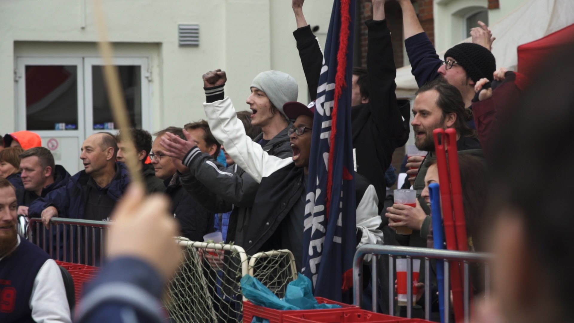 Mehrere Menschen jubeln energisch bei einem öffentlichen Ereignis. Einige tragen Schals und Mützen.