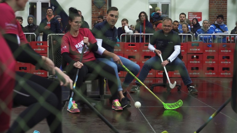 Mehrere Personen spielen Floorball auf einem nassen Platz, umgeben von Zuschauern.