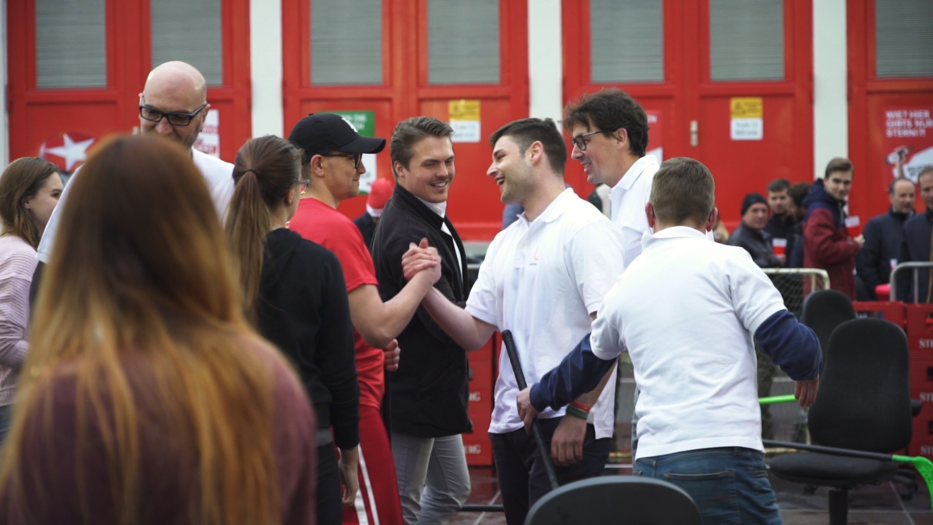 Mehrere Personen unterhalten sich vor einem Gebäude mit roten Türen.