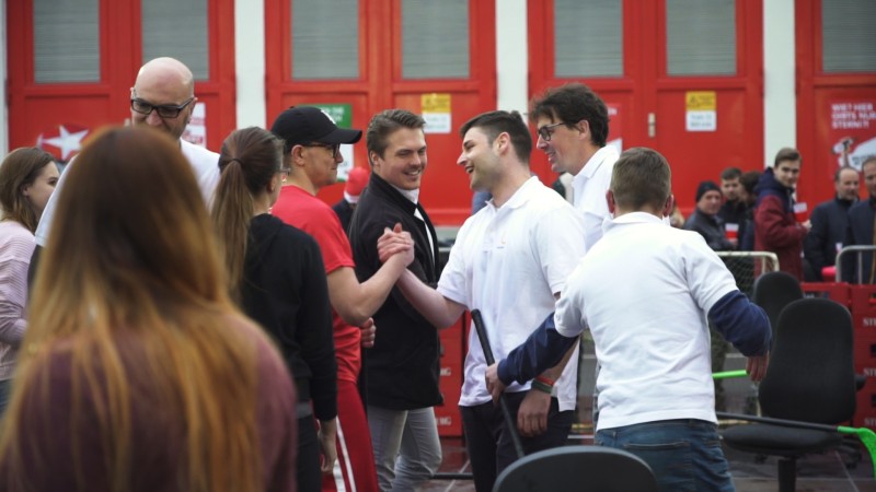 Mehrere Personen unterhalten sich vor einem Gebäude mit roten Türen.