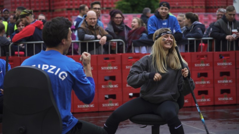 Ein Mann und eine Frau spielen Tauziehen bei einem öffentlichen Event und lachen dabei.