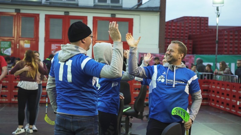 Drei Personen in Sportkleidung klatschen sich freudig ab bei einem Event im Freien.