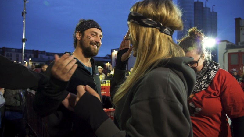 Zwei Personen lachen bei Dämmerung nebeneinander, umgeben von einer feierlichen Menge.