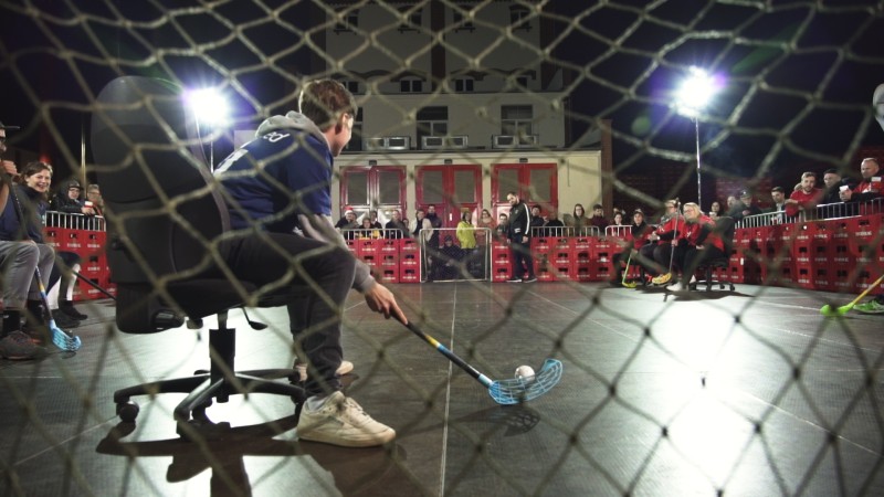 Ein junger Spieler spielt Floorball in einer Halle vor Zuschauern. Er zielt mit dem Schläger auf einen kleinen Ball.