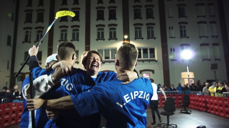 Vier Personen in blauen Jacken umarmen sich freudig bei Nacht vor einem Gebäude.