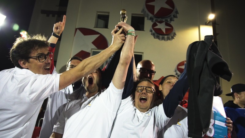 Eine Gruppe jubelnder Menschen hält gemeinsam einen Pokal hoch.