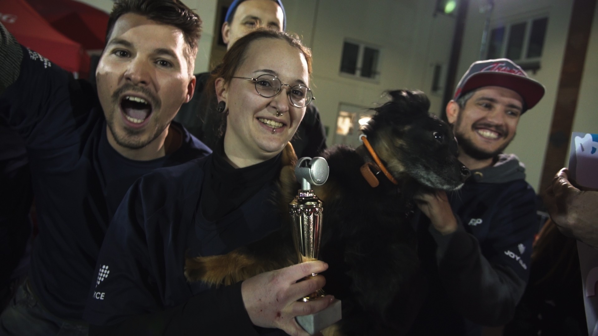 Vier Personen und ein Hund freuen sich und halten gemeinsam einen Pokal.