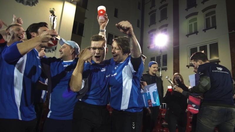 Eine Gruppe begeisterter Personen in Sporttrikots feiert nachts einen Sieg mit einem Pokal.