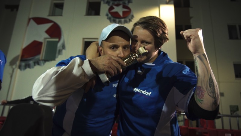 Zwei Fußballspieler feiern einen Sieg bei Nacht, einer trinkt aus einem Pokal.