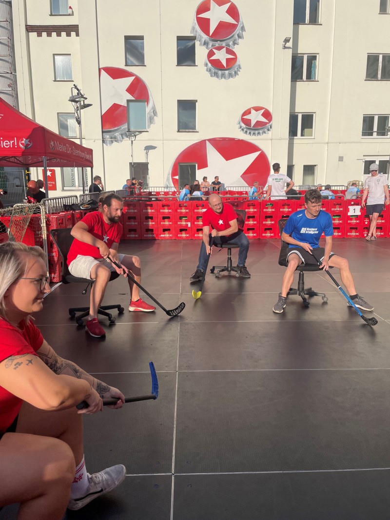 Vier Personen spielen auf Rollhockern im Freien eine Partie Hockey.
