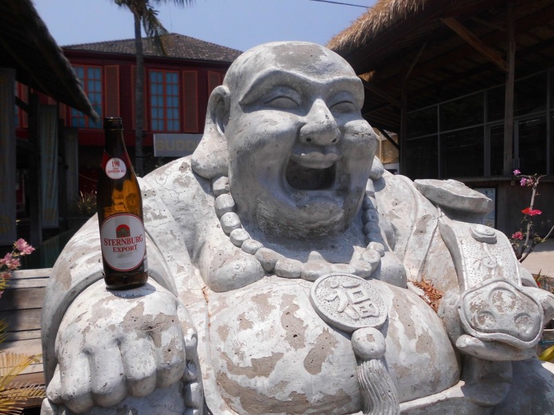 Eine Flasche Sternburg Export steht auf der rechten Hand einer steinernen Buddha-Figur.