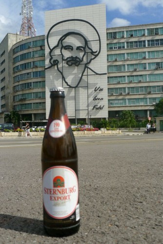 Eine Flasche Sternburg Export steht vor einem Gebäude mit einem großen Porträt von Fidel Castro.
