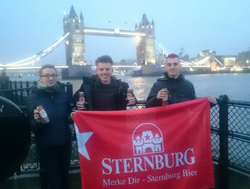 Drei Personen stehen mit Sternburg Dosen vor der Tower Bridge in London und halten eine große Sternburg-Flagge.