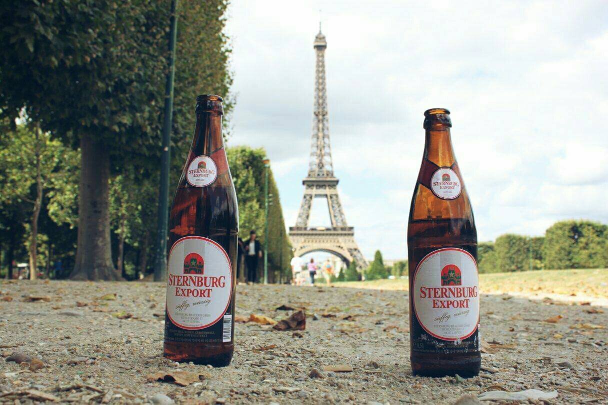 Zwei Flaschen Sternburg Export stehen auf einem Weg vor dem Eiffelturm in Paris.