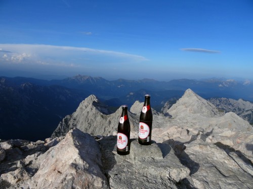 Zwei Flaschen Sternburg Export stehen auf einemBerggipfel mit Blick auf eine weite Berglandschaft unter blauem Himmel.
