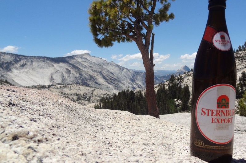 Eine Flasche Sternburg Export steht im Vordergrund vor einer Berglandschaft, im Hintergrund ein kleiner Wald.